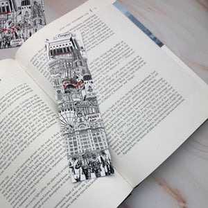 A black and white illustrated bookmark featuring Liverpool landmarks and sculptures with small red accents, shown resting on an open book page.