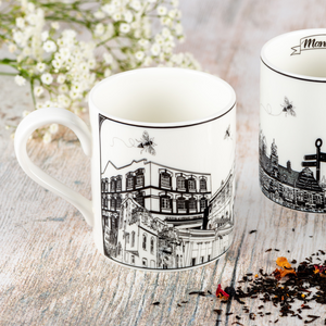 two white ceramic mugs featuring black and white illustrations of various famous landmarks around Manchester