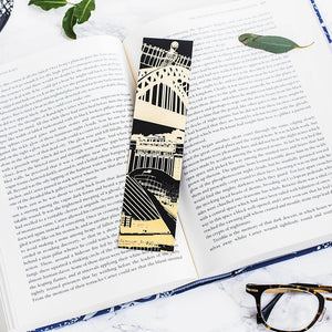 Newcaslte Landmarks bookmark pictured on top of an open book. The bookmark features famous Newcastle Landmarks in a black and gold design.