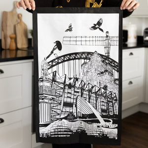 woman holing the powder butterfly newcastle tea towel featuring famous newcastle landmarks and icons in black/white