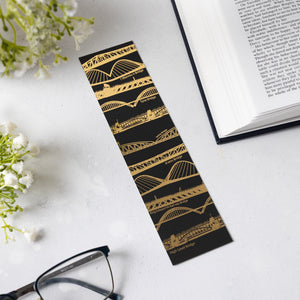 Bridges bookmark laid on a white surface next to white flowers an open book and a pair of black framed glasses.