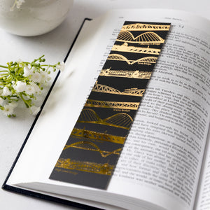 Bridges bookmark laid on an open book. On a white table witha white flower to the right.