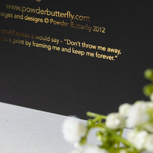 Black card with gold text and white flowers on a gray surface