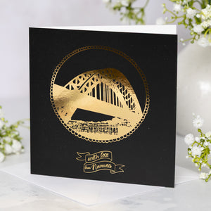 Black card with gold foil Tyne Bridge design and 'with love from Newcastle' text, surrounded by white flowers.