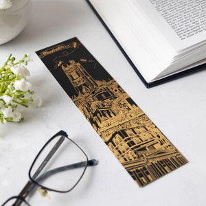 Decorative black soft-touch bookmark with gold foil Manchester-themed architectural design with glasses and next to an open book