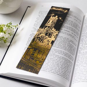 Decorative black soft-touch bookmark with gold foil Manchester-themed architectural design on an open book