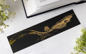 Northumberland-themed gift: Black and gold foil bookmark featuring the Sycamore Gap Tree on a white surface with an open book and glasses.