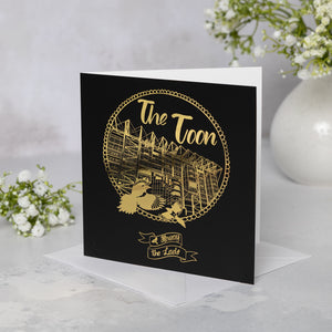 Black card with gold foil featuring St James' Park, two magpies, and the "Howay the Lads" design and text on a white surface with floral elements.