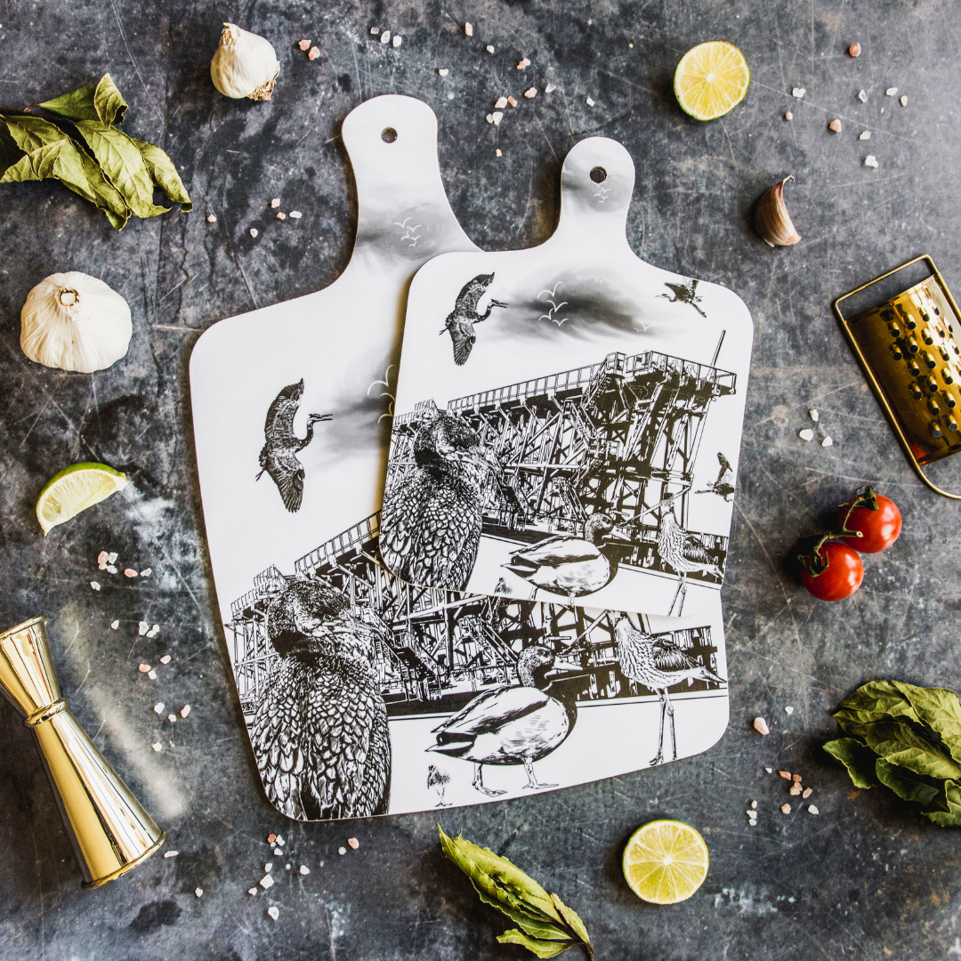 Powder Butterfly's Dunston Staiths themed chopping board over with a decorative background featuring food items.