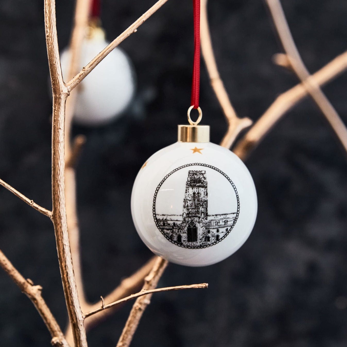 White ceramic bauble featuring a black and white illustration of Durham cathedral complete with gold trim and red ribbon by powder butterfly