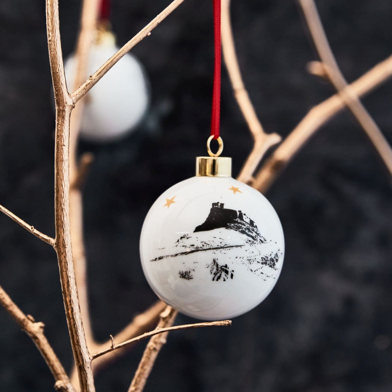 White Ceramic holiday ornament of lindisfarne illustrated in black and white, complete with gold trim and red ribbon