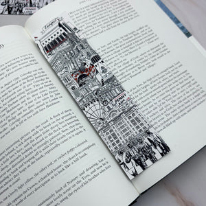 A black and white illustrated bookmark featuring Liverpool landmarks and sculptures with small red accents, shown resting on an open book page.