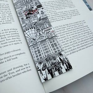 A black and white illustrated bookmark featuring Liverpool landmarks and sculptures with small red accents, shown resting on an open book page. Featuring The Beatles and Penny Lane road sign. 