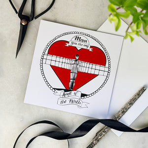 Greeting card with Angel of the North big red heart design on a white surface with scissors and ribbon