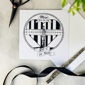 Black and white illustration of the Angel of the North on a card with scissors and ribbon on a light surface.