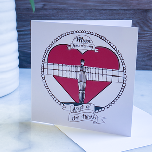 Card with a heart design featuring the Angel of the North and text, with a wooden background on a marble surface.