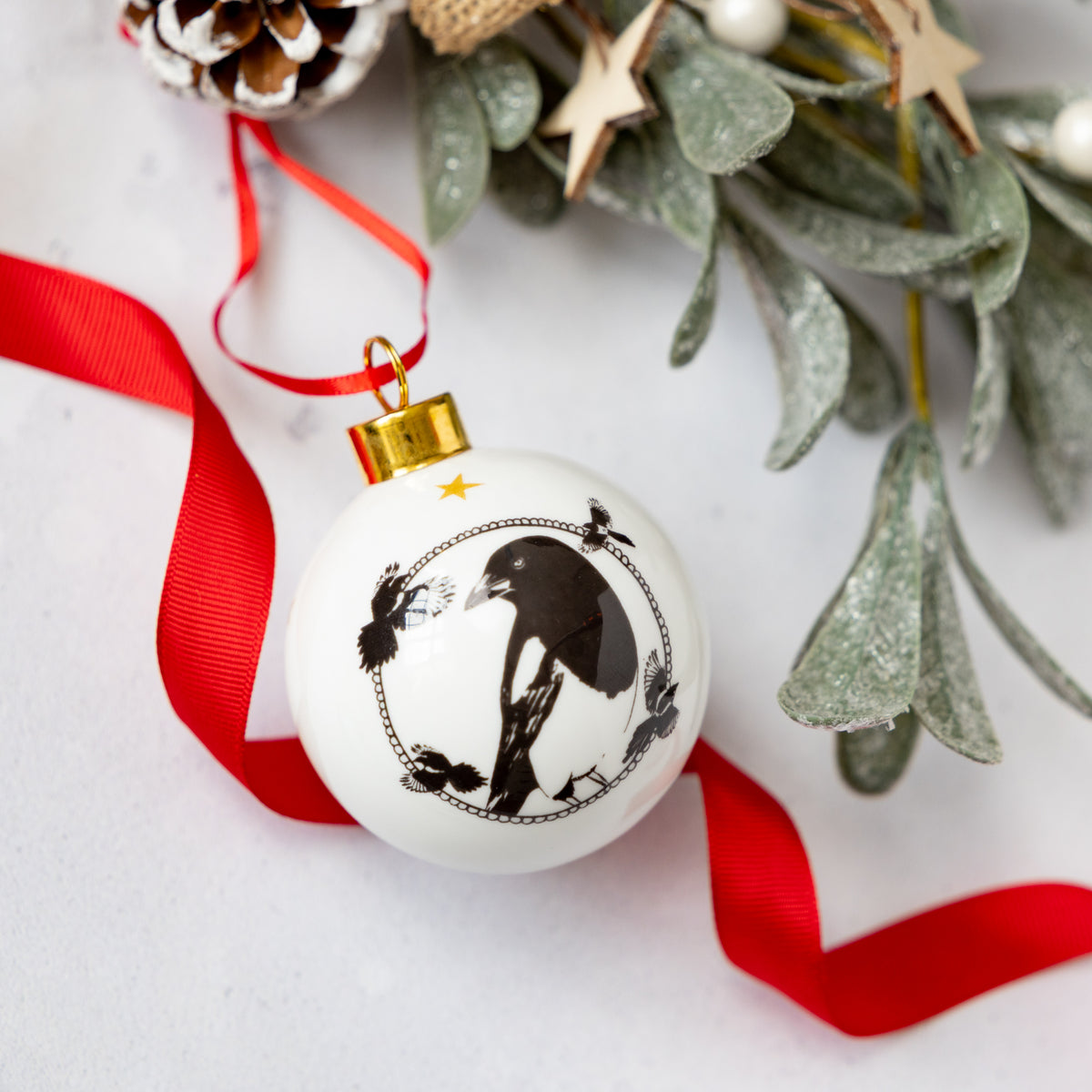 Black and white enamel bauble illustrated with a magpie in black and white and gold trim