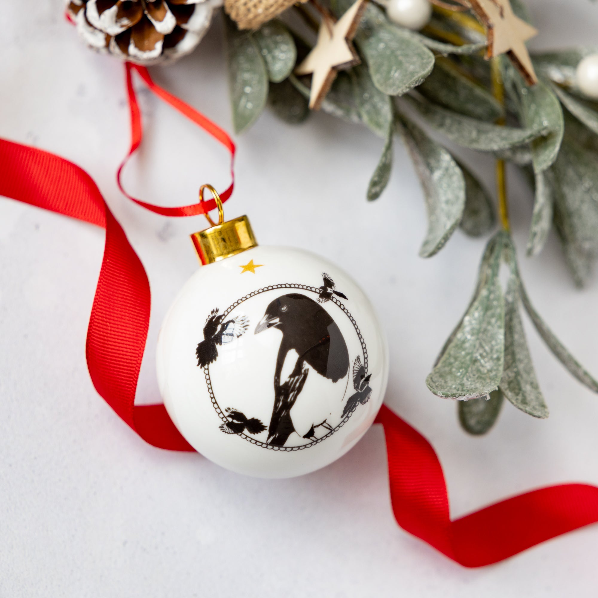 Black and white enamel bauble illustrated with a magpie in black and white and gold trim