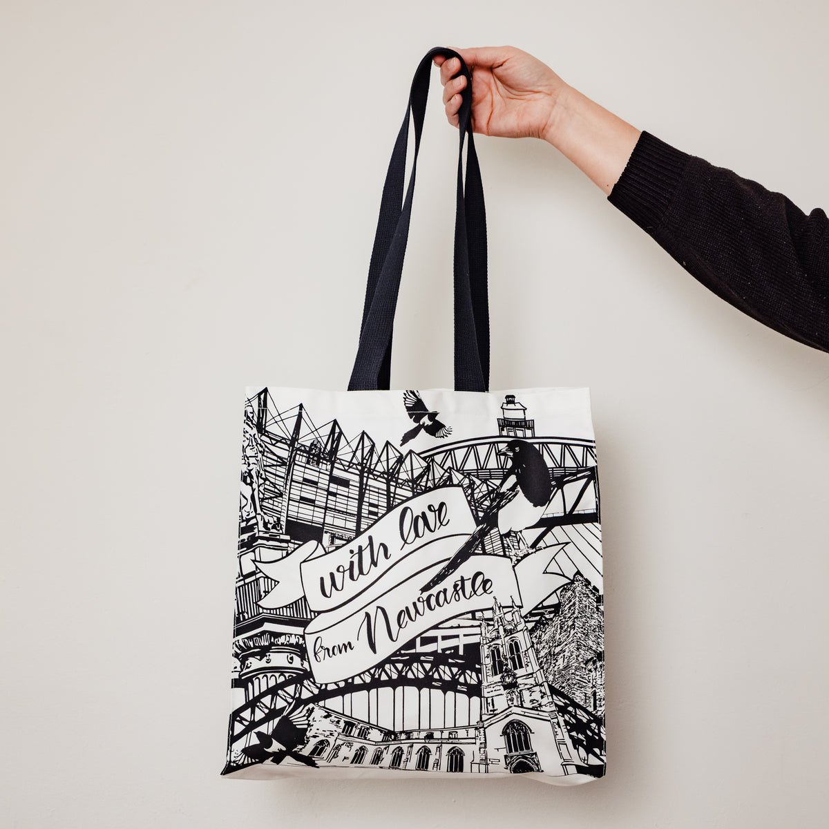 Someone holding up the newcastle landmarks tote bag by powder butterfly illustrated in black and white