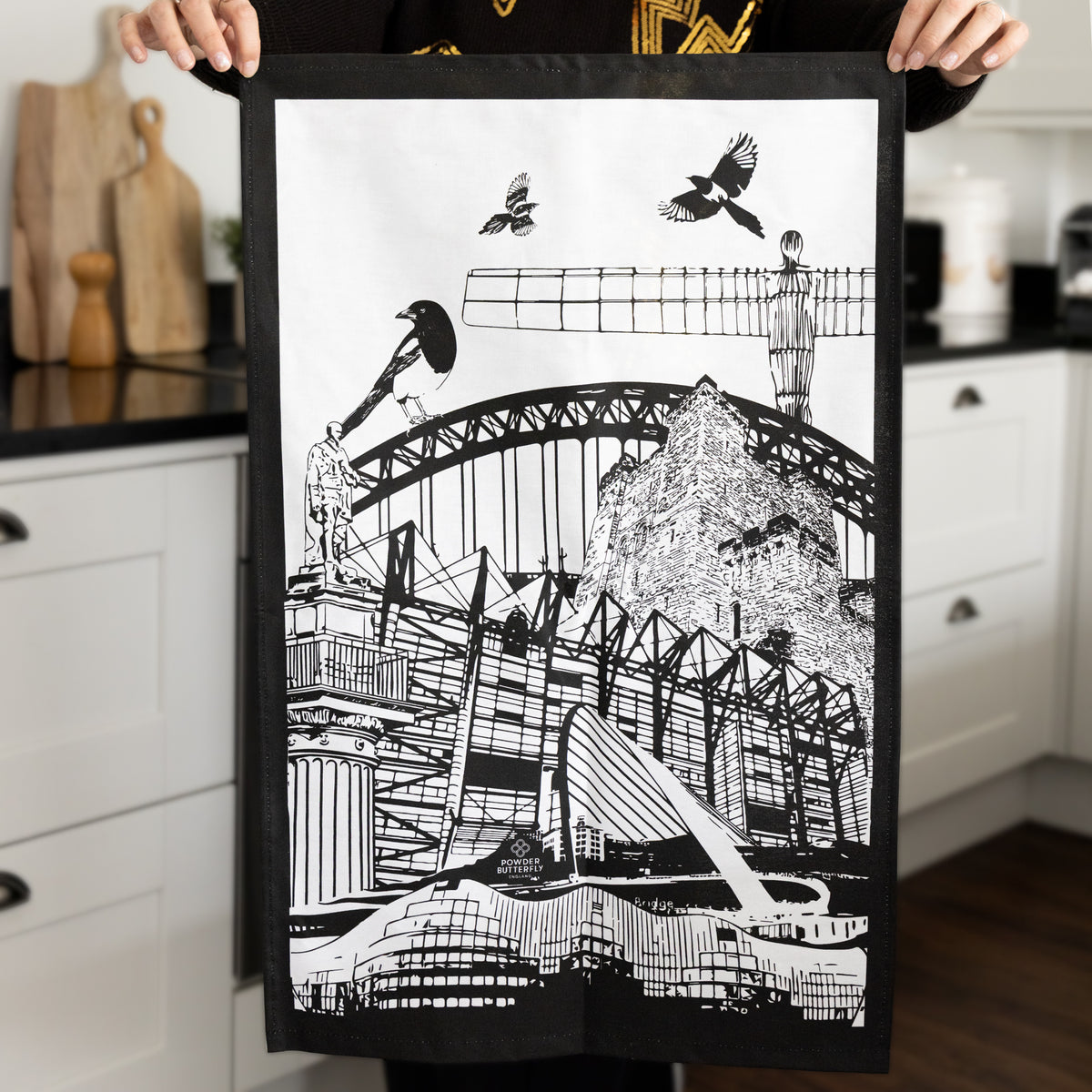 woman holing the powder butterfly newcastle tea towel featuring famous newcastle landmarks and icons in black/white