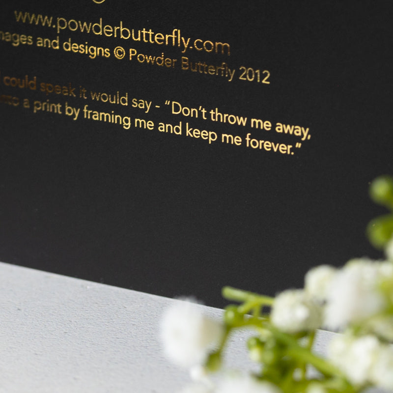 Black card with gold text and white flowers on a gray surface