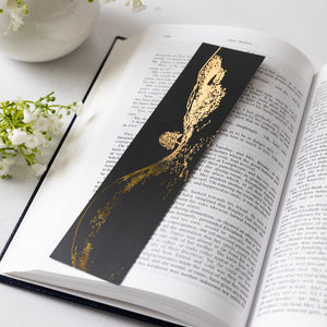 Black and gold bookmark with illustration of Sycamore Gap tree on an open book with flowers in the background
