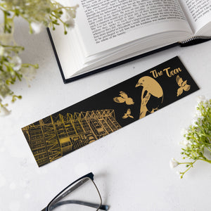 Black and gold bookmark with illustrations on a white surface with an open book and glasses.