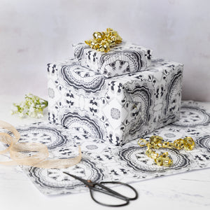 Gift box wrapped in black and white patterned Newcastle-themed paper with scissors and gold ribbons on a light background