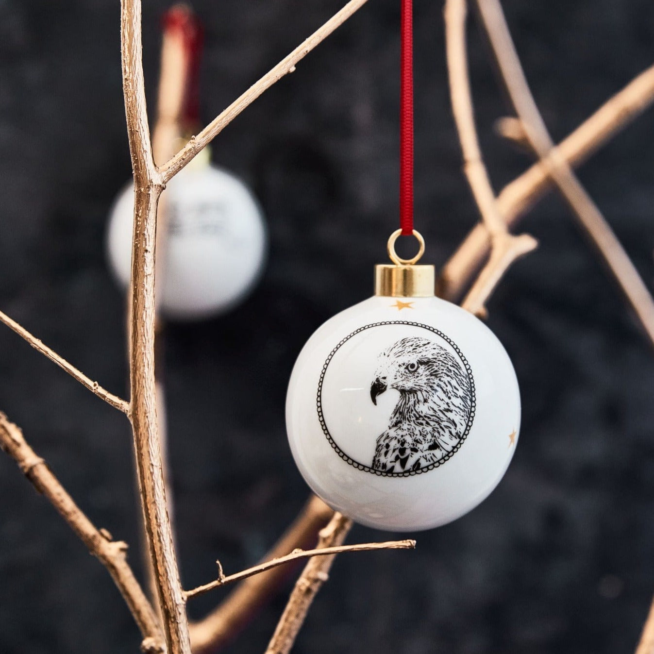 White ceramic holiday ornament featuring a black and white illustration of the red kite by powder butterfly the deign is completed with a red ribbon to hang and gold trim
